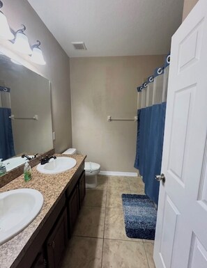 Une salle de bain avec deux lavabos, des toilettes, une douche avec un rideau bleu et une porte.
