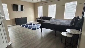 Ein Schlafzimmer mit Bett, Deckenventilator, einem an der Wand befestigten Fernseher und einem Fenster mit Jalousien.