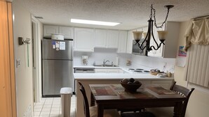 A kitchen with white cabinets, a stainless steel refrigerator, a coffee maker, and a dining table with chairs. - Oceanfront condo in Pinnicle Port on the west end of Panama City Beach. (Panama City)