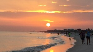 A beach scene with the sun setting over the horizon, people walking along the shore, and a calm sea. - Oceanfront condo in Pinnicle Port on the west end of Panama City Beach. (Panama City)