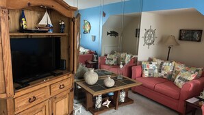 A living room with a wooden cabinet, a flat-screen TV, a red sofa, and a coffee table with decorative items. - Oceanfront condo in Pinnicle Port on the west end of Panama City Beach. (Panama City)
