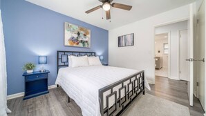 A bedroom with a bed, a nightstand, a ceiling fan, and artwork on the walls. - Golden Racehorse MCM 3BR Slps 6 - 7 Min to Oaklawn (Hot Springs)