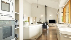 A modern kitchen with built-in appliances, a central island, and a dining area with a black sofa. - Hanging Garden On Mernda- Mountain view retreat  (Olinda)
