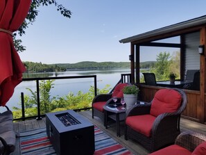 Une terrasse dotée de meubles en osier, d’un barbecue et offrant une vue sur un lac.