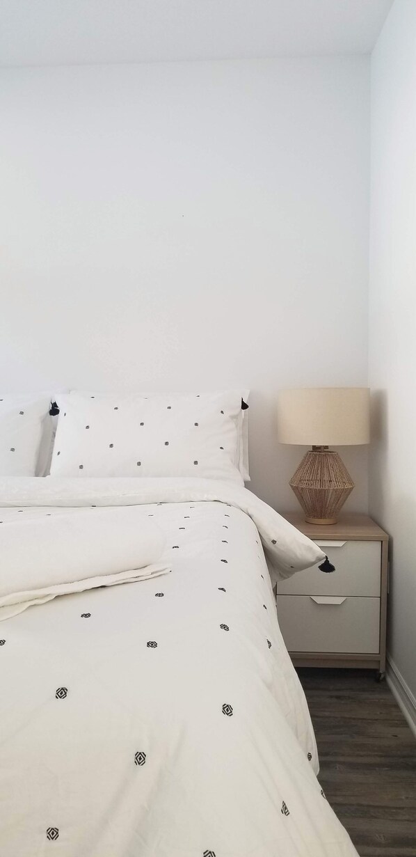A neatly made bed with a patterned duvet and pillows, a bedside table with a lamp, and a drawer. - The Kubo Chalet (Lac-des-Loups)