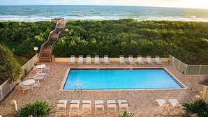 A pool area with a view of the ocean, surrounded by greenery and equipped with sun loungers and a staircase leading to a deck. - The Sea Turtle at Spoonbill Resort Villa (Stuart)