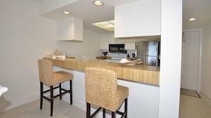 A modern kitchen with two wicker chairs, a wooden countertop, and white cabinets. - The Sea Turtle at Spoonbill Resort Villa (Stuart)