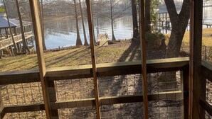 Uitzicht vanaf een overdekt terras op een meer, met een houten terras en een prieeltje op de achtergrond.