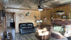Een gezellige woonkamer met een leren bank, een fauteuil, een open haard en houten wanden.
