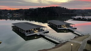 Dos barcos amarrados con estructuras adosadas, un lago tranquilo y un puente al fondo.