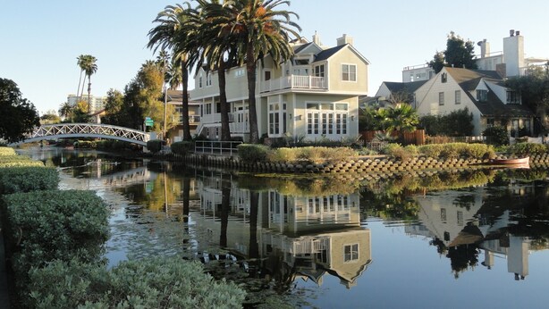 Una propiedad frente al agua con una casa grande, un puente y un lago tranquilo que refleja el entorno.