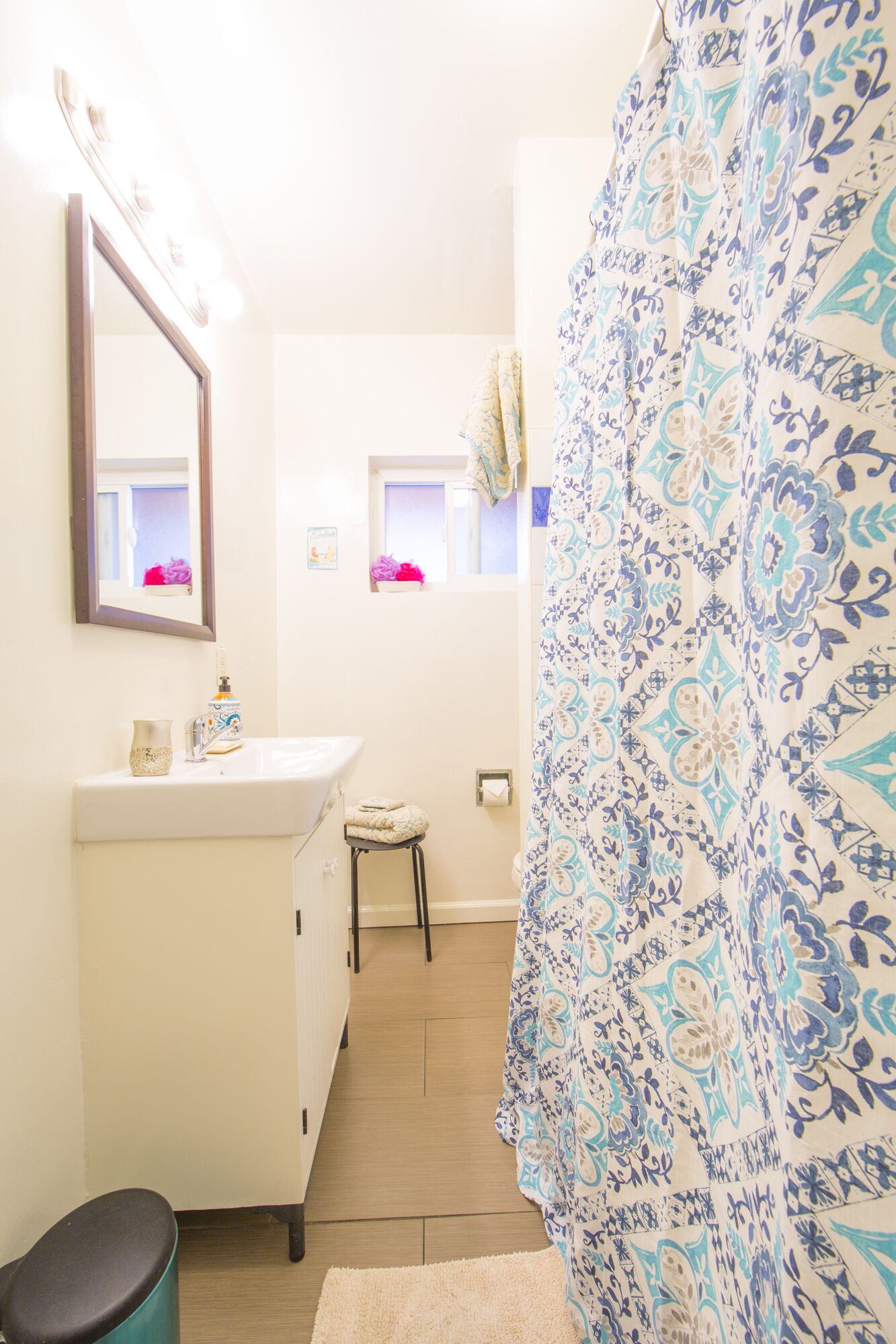 Un baño con lavamanos blanco, un espejo, toallero y cortina de ducha con diseño azul y blanco.
