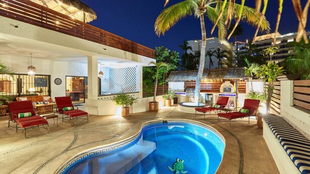 A swimming pool with red lounge chairs and a turtle, surrounded by palm trees and a thatched roof structure. - Casa Mismos w/pool |Walk to Medano Beach + Marina (Cabo San Lucas)