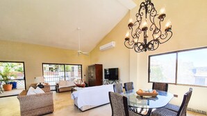 A spacious living room with a glass dining table, wicker furniture, a ceiling fan, and a large window. - Casa Mismos w/pool |Walk to Medano Beach + Marina (Cabo San Lucas)