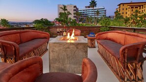 A rooftop terrace with leather sofas, a central fire pit, and a view of city buildings. - Casa Mismos w/pool |Walk to Medano Beach + Marina (Cabo San Lucas)
