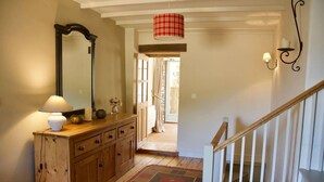 Un couloir avec une commode en bois, un miroir, une lampe, un luminaire suspendu à carreaux rouges et un escalier.