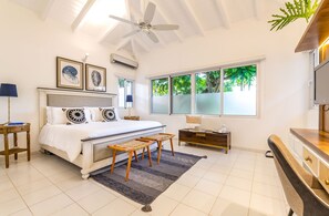 Relax in this serene bedroom with a large bed, ceiling fan, and a window offering a view of lush greenery.