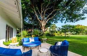 Relax in a serene garden setting with a comfortable sofa and chairs, surrounded by lush greenery and a large tree.