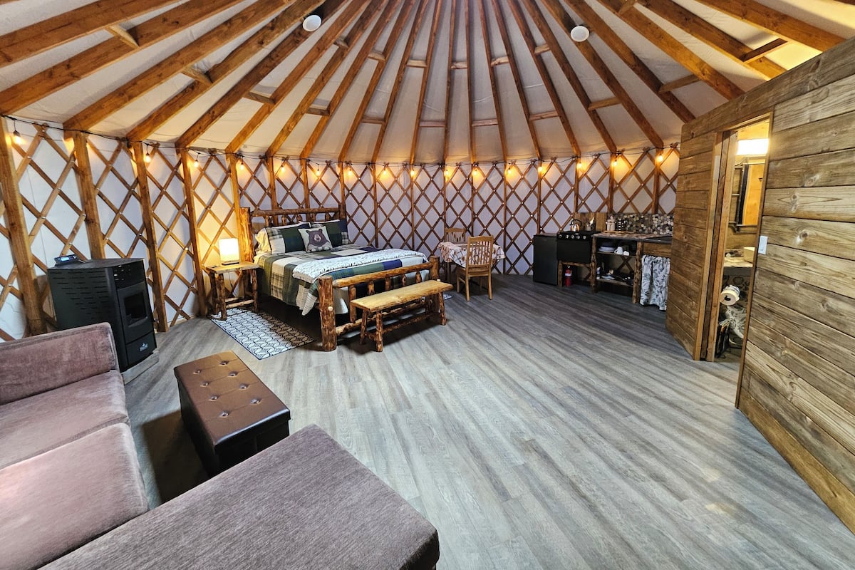 A yurt interior with a bed, seating area, and a small kitchenette.