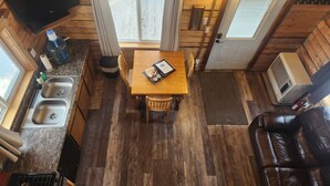 A compact cabin with a wooden interior, a dining area with a table and chairs, a kitchenette with a sink and stove, and a large window.