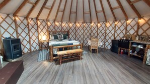 A cozy interior with a wooden bed, a small table, a bench, and a kitchen area.