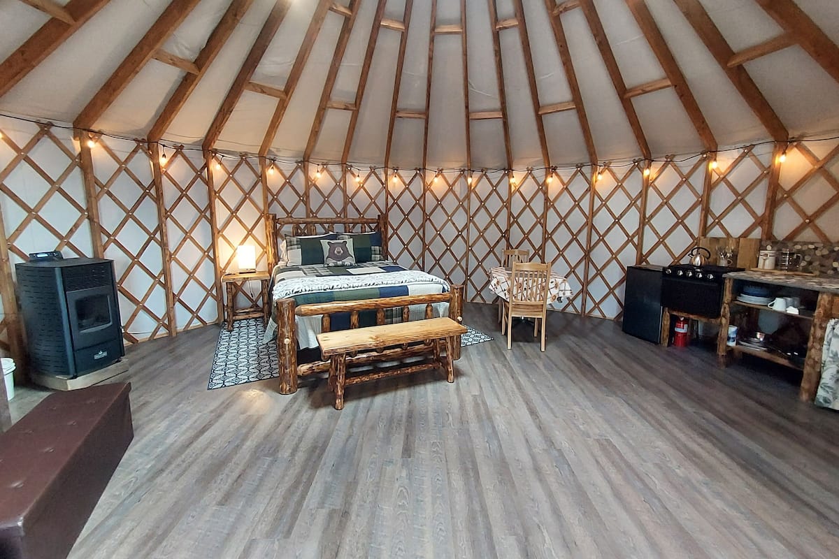 A cozy interior with a wooden bed, a small table, a bench, and a kitchen area.