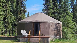 A large, single-story tent with a covered porch, two white Adirondack chairs, and a wooden bench.