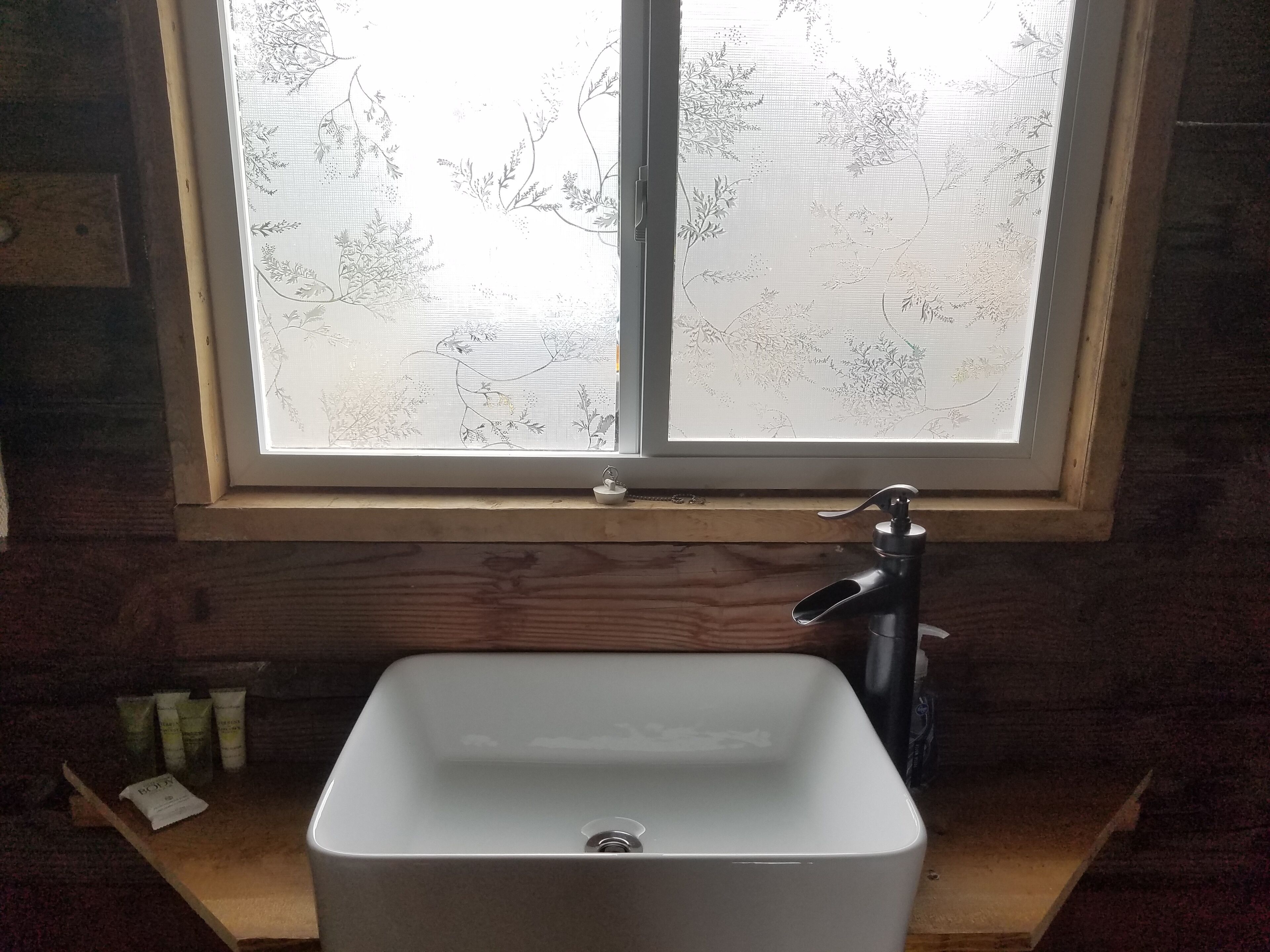 A bathroom with a window featuring a frosted glass design, a white sink, and a black faucet.