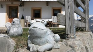 A stone frog sculpture in front of a chalet with a wooden fence, a dining table, and chairs. - Lamplberg by Interhome (Hippach)