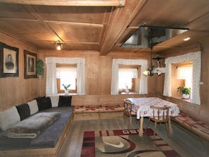 A cozy room with a wooden ceiling, a sofa with cushions, a dining table with chairs, and a patterned rug.