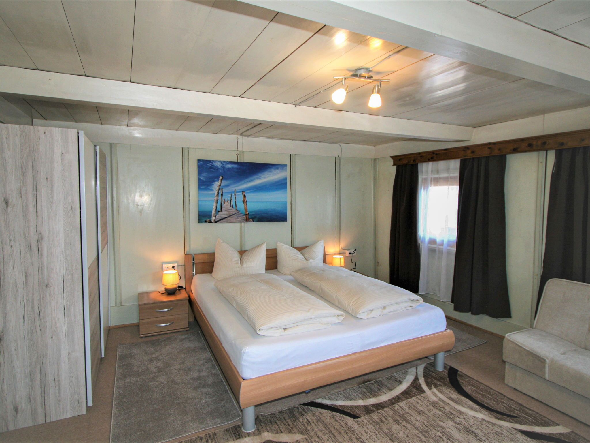 Une chambre à coucher moderne avec un lit en bois, des lampes de chevet, un tableau et une vue sur l’extérieur.