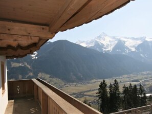 Un balcón de madera con vistas a montañas nevadas y un valle en la distancia.