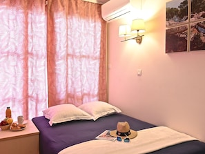 A bedroom with a bed, pillows, a nightstand with a bottle and fruit, and a wall-mounted lamp.