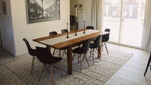 A dining area with a wooden table, black chairs, a patterned rug, a large window with a view, and a framed cityscape picture on the wall. - The Desert Sunset: 4 BDR, 5 Beds, Fast Wifi, Large TV, Large private pool, (Mesa)