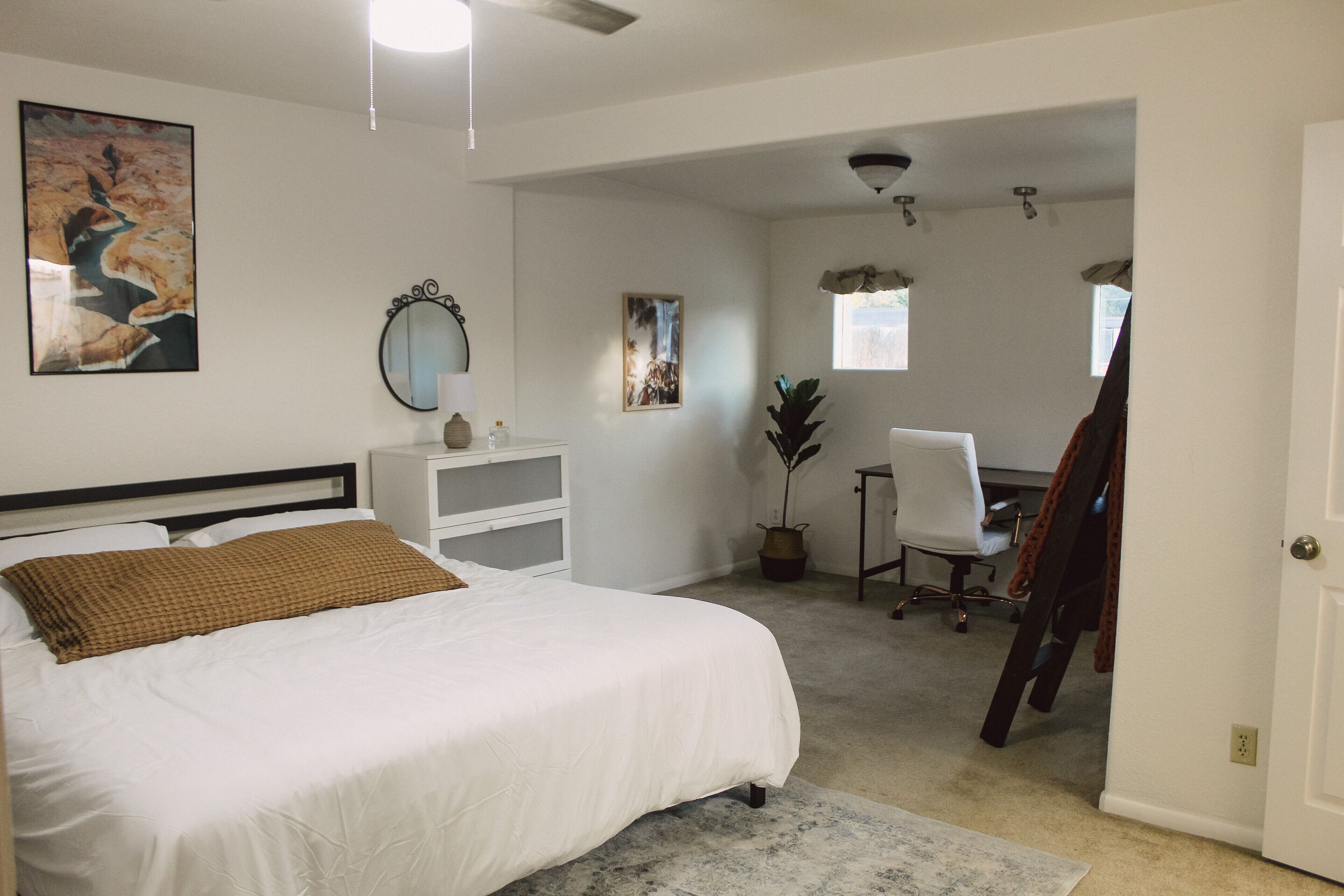 A bedroom with a large bed, a desk, a chair, and a potted plant.