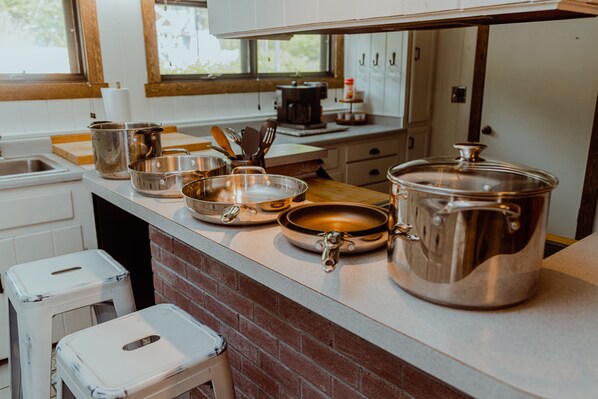 A kitchen with stainless steel cookware, a coffee maker, and a brick backsplash.