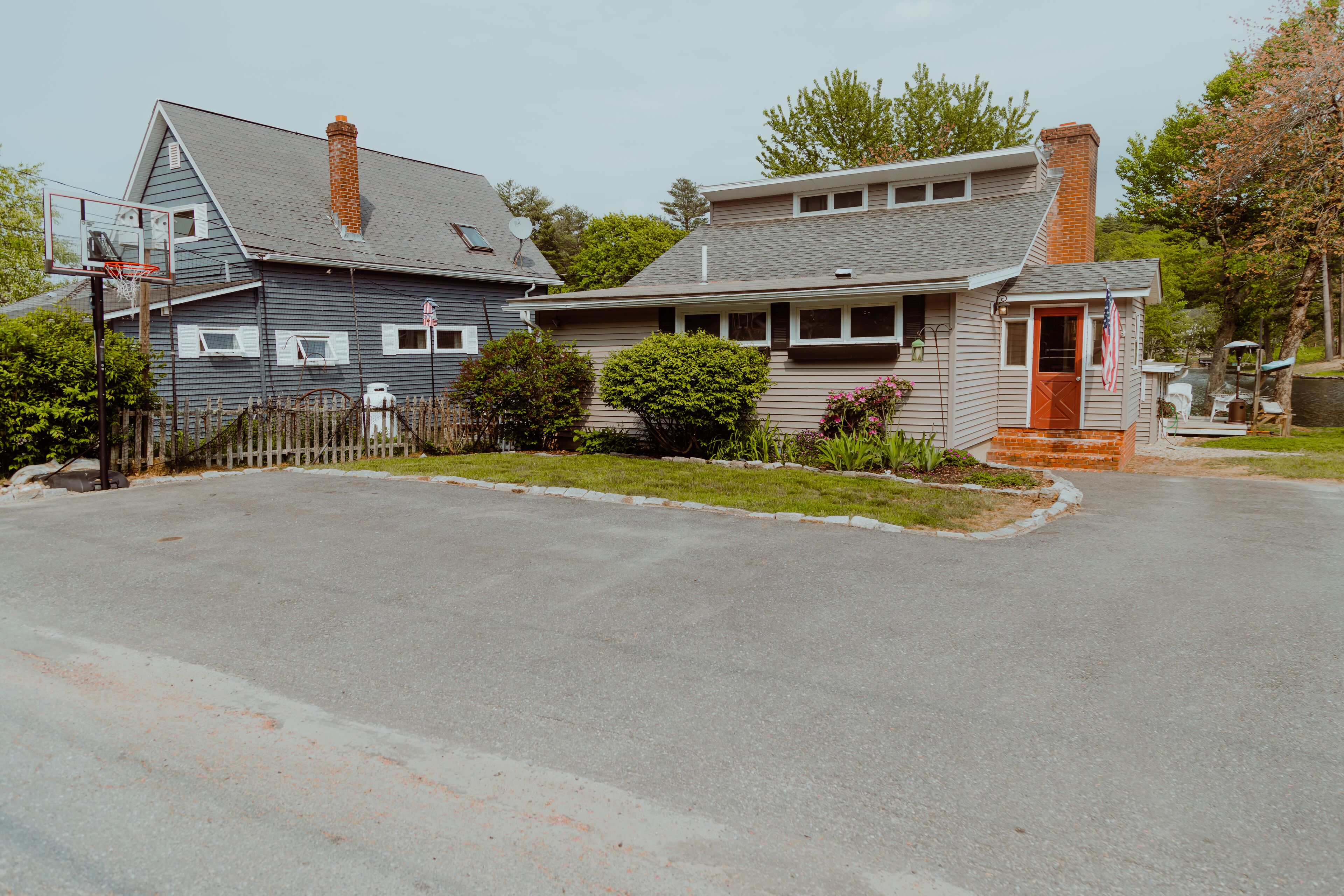 A residential street with two houses, one with a visible basketball hoop and a small front yard.
