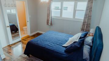 Un dormitorio con cama, ventilador de techo, ventana con cortinas y puerta que da a un baño.