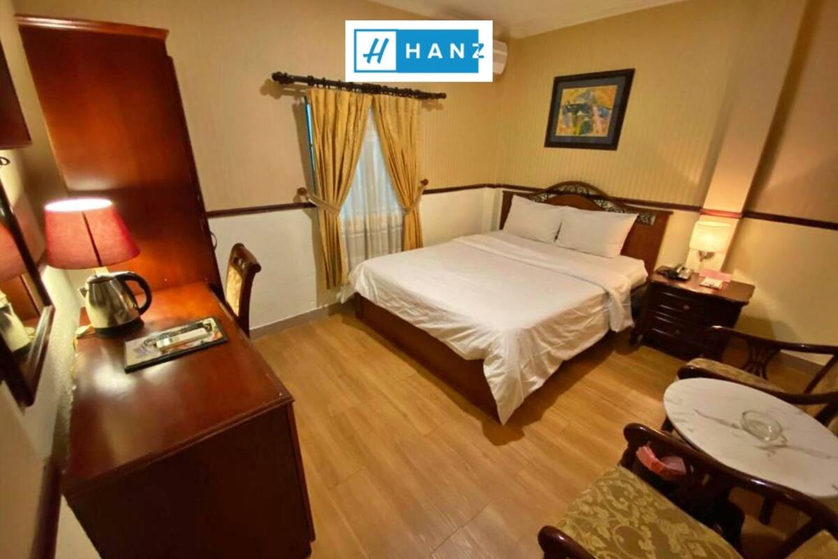 A hotel room with a bed, bedside table, lamp, and a small table with a chair.