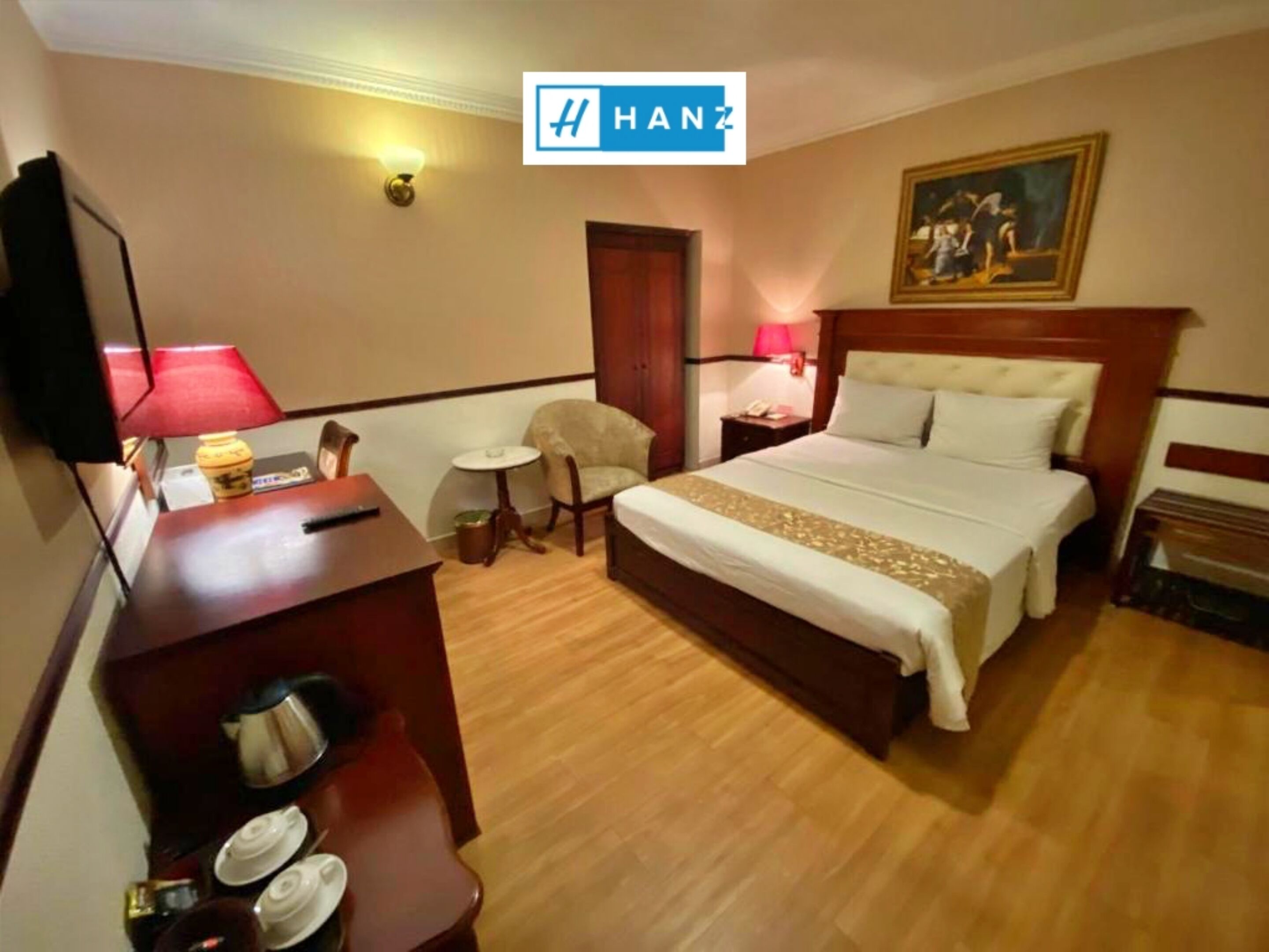 Una habitación de hotel con una cama, un escritorio, una silla, una mesita y un cuadro en la pared.