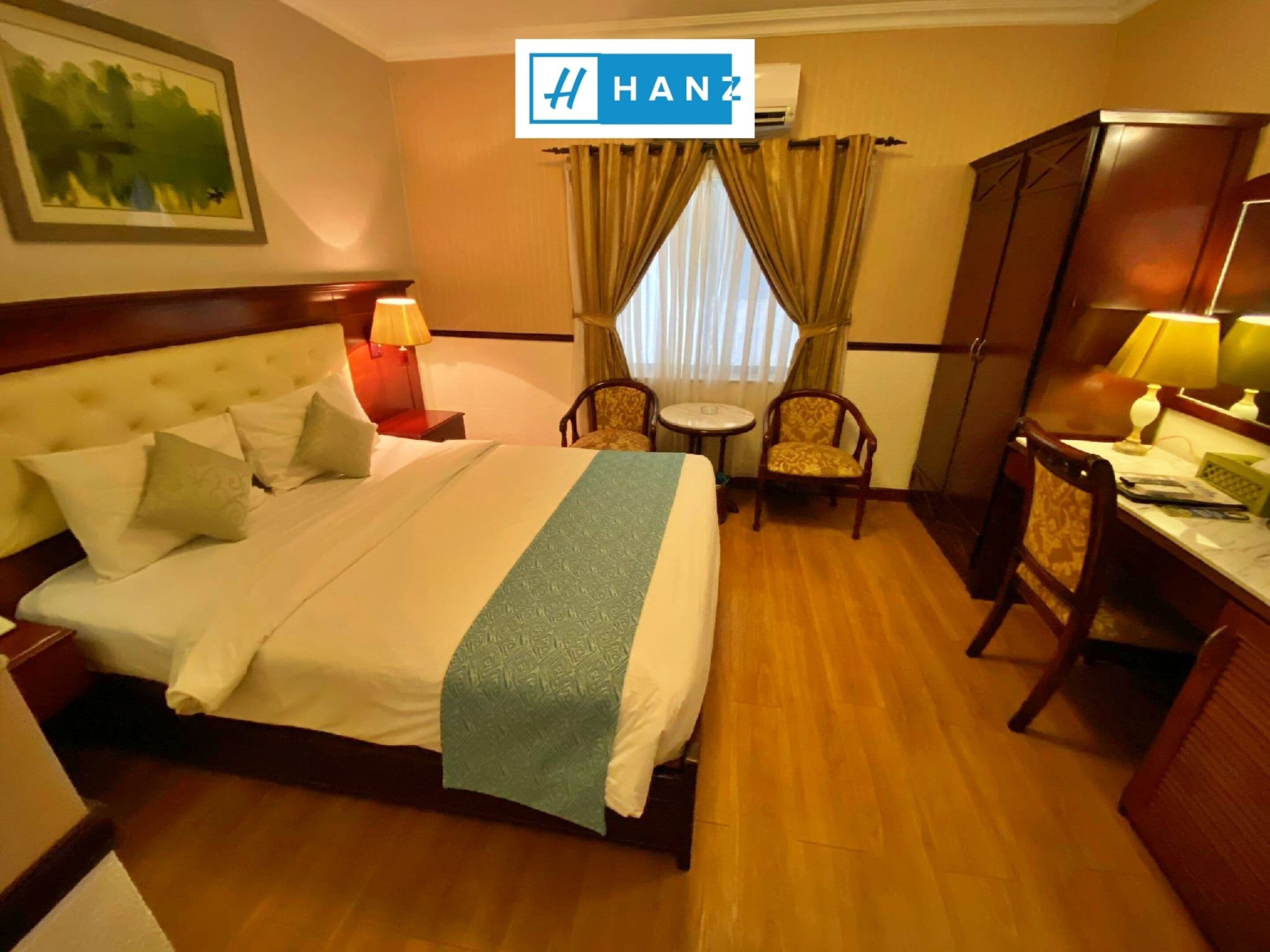 Hotelkamer met een groot bed, een bureau, twee stoelen, een kleine tafel en een raam met gordijnen.
