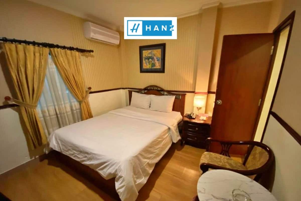 A hotel room with a bed, bedside table, lamp, and a small round table with a glass on it.
