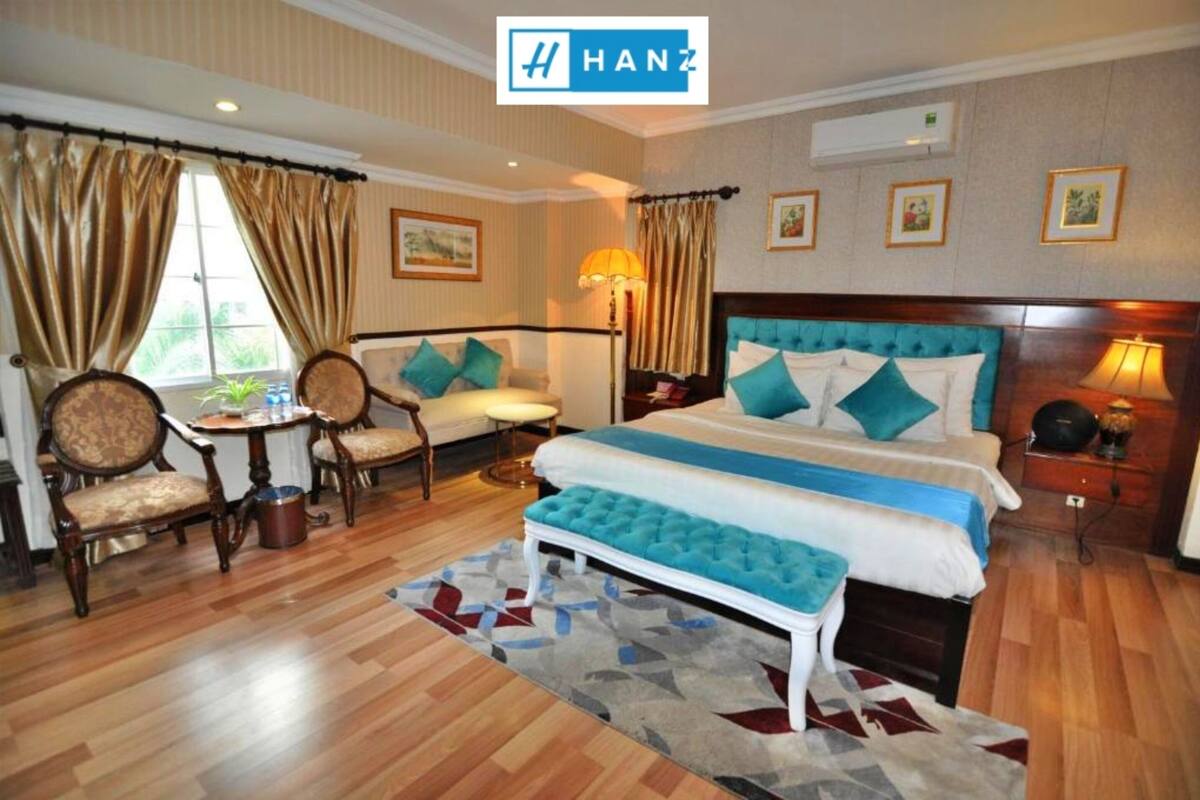 A hotel room with a large bed, two chairs, a small table, and a bench.