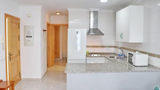 A kitchen with white cabinets, a stainless steel range hood, a granite countertop, a built-in oven, a microwave, and a sink. - First floor Apartment Santa Teresa (Conil de la Frontera)