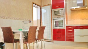 Eine moderne Küche mit roten und weißen Schränken, einer Mikrowelle, einem Backofen und einem Essbereich mit einem Glastisch und Stühlen.