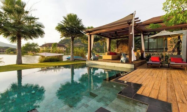 Una piscina con muelle de madera, sillas de descanso y una pérgola.