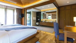 Un dormitorio con cama, escritorio, silla, televisión y un baño visible a través de una puerta abierta.