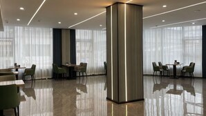 Een moderne hotellobby met een gepolijste vloer, een centrale kolom en een zithoek met tafels en stoelen.