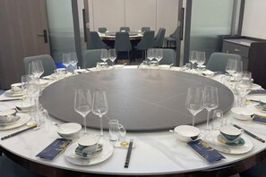 Un salón de conferencias con una mesa redonda dispuesta para una reunión, equipado con sillas, platos, vasos y cubiertos.