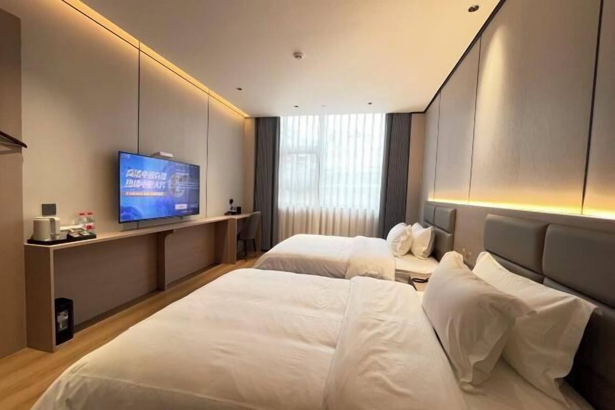 Habitación de hotel con dos camas, un televisor en la pared, un escritorio y una ventana con cortinas.